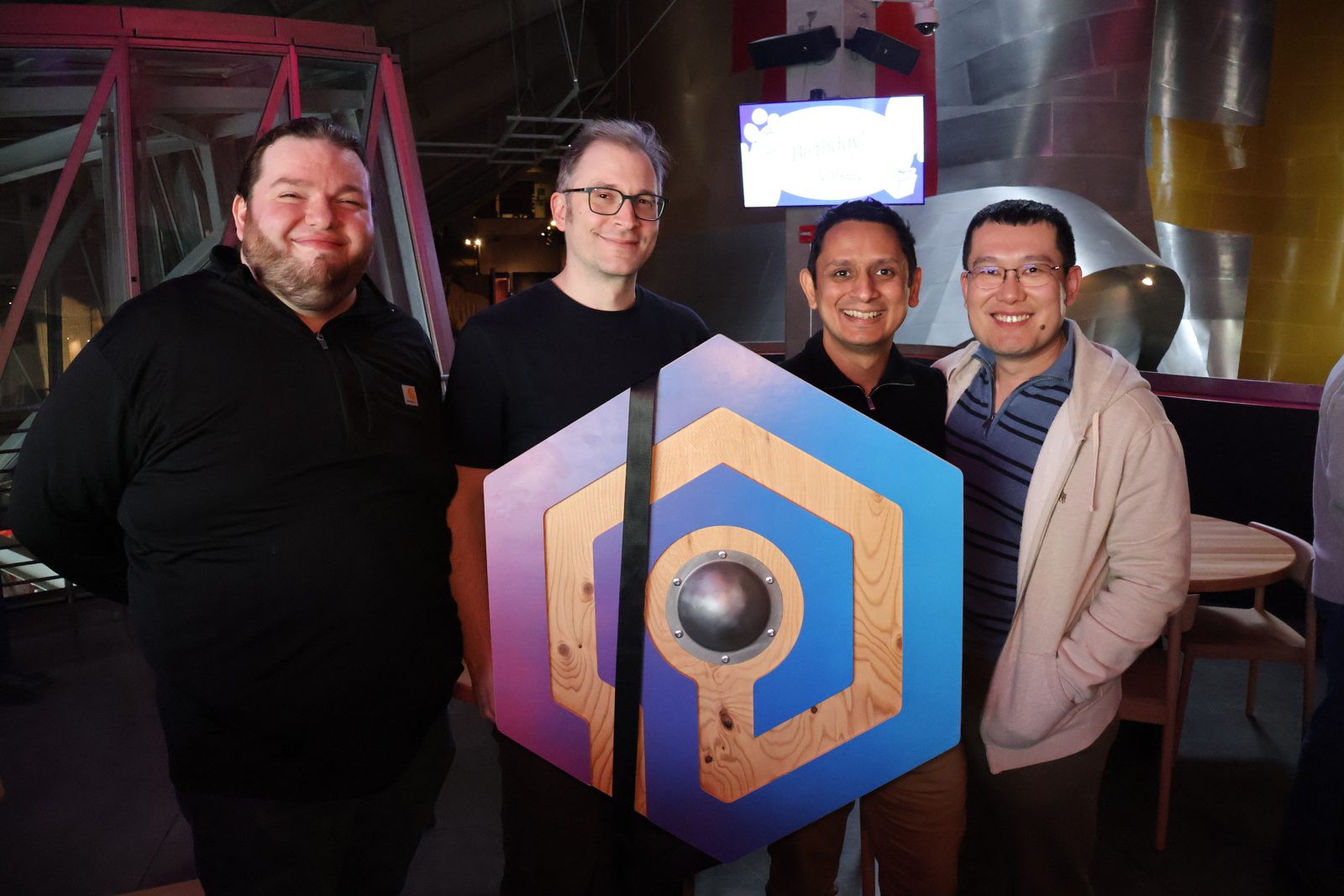 Contributors posing with a wooden Valkey logo at the birthday celebration
